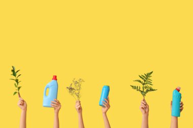 Deterjan şişeleri ve sarı arka planda bitki dalları olan birçok kadın eli.