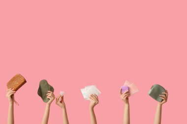 Farklı kadın hijyen ürünlerine ve pembe arka planda kozmetik çantalara sahip kadın elleri