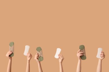 Bej arka planda regl ve yeniden kullanılabilir pedleri olan birçok kadın eli