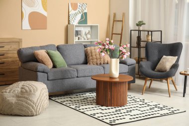 Kanepe, koltuk ve çiçek açan manolya dalları oturma odasının içindeki sehpanın üzerindeki vazoda.