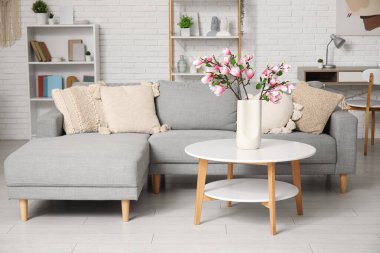 Konforlu kanepe ve çiçek açan manolya dalları oturma odasının içindeki sehpanın üzerindeki vazoda.