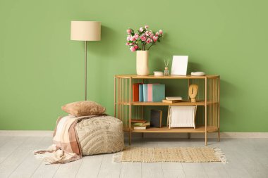 Pouf, vazoda yeşil duvarın yanında çiçek açan manolya dalları ve dekorasyonu olan raf ünitesi.