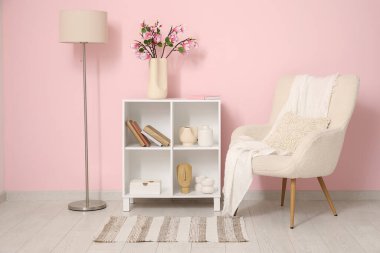 Koltuk ve raf ünitesi. Odada pembe duvarın yanında çiçek açan manolya dalları var.