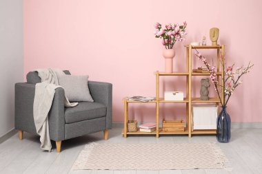 Koltuk ve raf ünitesi. Odada pembe duvarın yanında çiçek açan bahar dalları var.