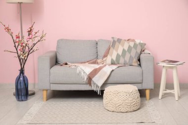 Konforlu kanepe, sehpa ve pembe duvarın yanında çiçek açan ağaç dalları.