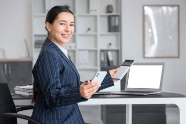 Cep telefonu ve hesap makinesi olan genç bir iş kadını ofiste rapor hazırlıyor.