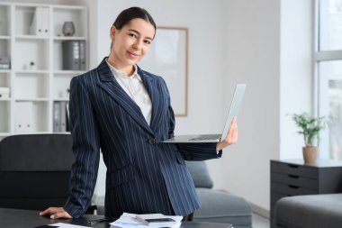 Dizüstü bilgisayarı olan genç iş kadını ofiste çalışıyor.