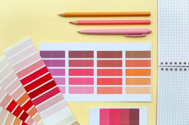 Farklı renk paletleri, not defteri, kalemler ve sarı arkaplanda kalem içeren kompozisyon