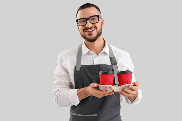 Молодой бариста с бумажными чашками кофе на сером фоне