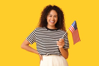 Sarı arka planda Amerikan bayrağı olan genç Afro-Amerikalı kadın.