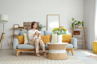 Güzel genç bayan kanepede otururken çay içiyor.