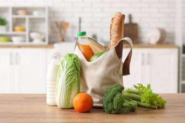 Mutfaktaki ahşap masada farklı taze ürünler bulunan market poşeti.