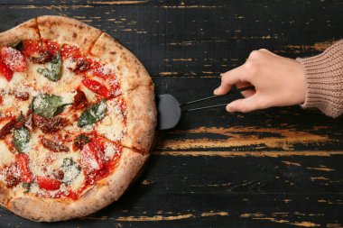 Kadın eli, siyah ahşap arka planda lezzetli bir pizza dilimi alıyor. Üst görünüm