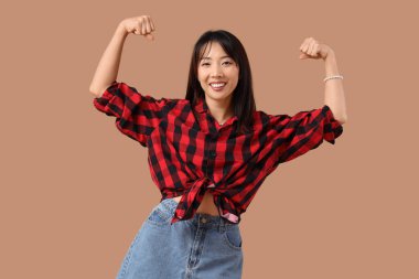Güzel genç mutlu Asyalı kadın bej arka planda kaslarını gösteriyor. Kadın Tarihi Ayı