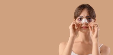 Bandajlı burnu ve bej arka planda morlukları olan genç bir kadın. Mesaj için yeri var. Estetik ameliyat konsepti