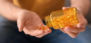 Kavanozda balık yağı kapsülleri olan genç adam, yakın plan.