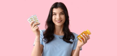 Güzel, mutlu, genç bir kadın. Kavanozu ve pembe arka planda balık yağı kapsülleri var.