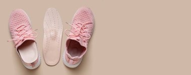 Bej arkaplan üzerinde ortopedik tabanlı ve metin için yeri olan bir çift şık pembe spor ayakkabı.