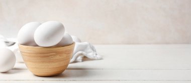 Beyaz ahşap masada çiğ tavuk yumurtası ile kase. Tasarım için pankart