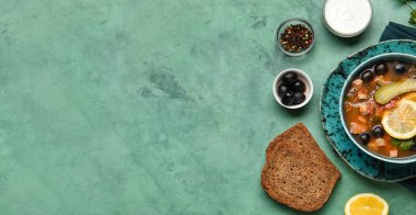 Bir kase lezzetli hodgepodge çorbası, ekmek, baharatlar ve yeşil arka planda ekşi krema.