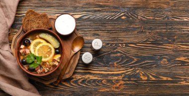 Bowl of tasty hodgepodge soup, spices, bread and sour cream on wooden background with space for text, top view clipart