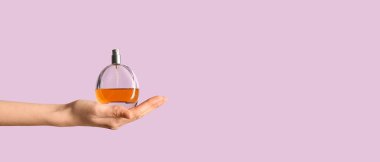 Leylak arka planında parfüm şişesi olan bir kadın el.