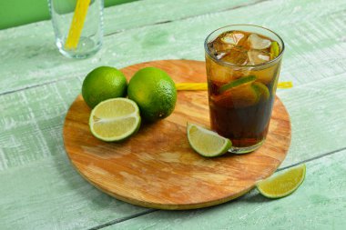 Bir bardak soğuk Küba Libre kokteyli ve yeşil ahşap masada limon.