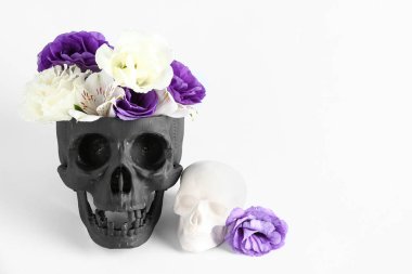 Beyaz arka planda güzel çiçekler olan siyah insan kafatası.