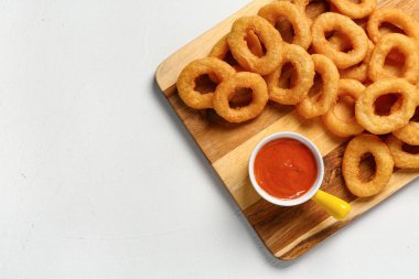 Wooden board with fried breaded onion rings and sauce on white background