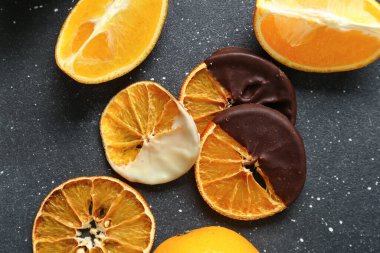 Çikolata soslu kurumuş portakal dilimleri siyah arka planda.