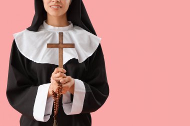Pembe arka planda haçlı ve boncuklu genç rahibe