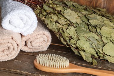 Masaj fırçası, temiz havlular ve ahşap arka planda huş ağacı saunası, yakın plan.