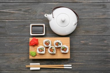 Soya soslu lezzetli suşi ruloları, yemek çubukları ve ahşap zemin üzerinde çaydanlık.