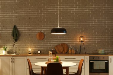 Parlayan lambalar, beyaz tezgahlar, fırın ve akşam yemeği masası olan mutfağın içi.