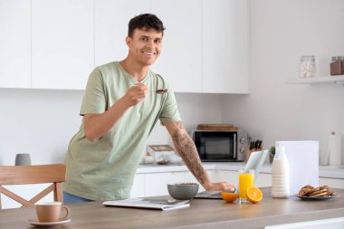 Dizüstü bilgisayarlı genç adam mutfakta mısır topu yiyor.