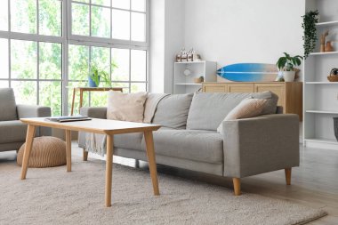 Oturma odasının içinde kanepeler, masa ve sörf tahtası var.