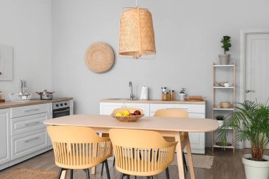 Yemek masası, sandalye, beyaz tezgah ve lamba olan şık bir mutfak.