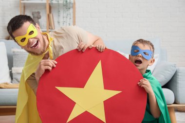 Küçük çocuk ve babası süper kahraman kostümlü ve evinde kağıt kalkan var.