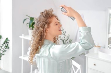 Evdeki banyoya saç spreyi sıkan genç ve güzel bir kadın.