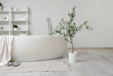 Küveti, raf ünitesi ve zeytin ağacı olan şık bir banyo.