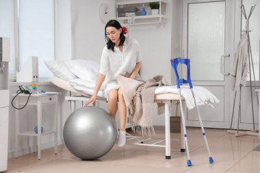 Hastane koğuşunda yatağında oturan spor topu olan bir kadın hasta.