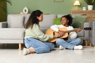 Genç ve güzel mutlu Afro-Amerikan anne ve kızı evde gitar çalıyorlar.