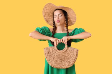 Hasır şapkalı, sarı arka planda öpücük saçan güzel bir kadın.