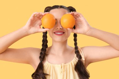 Sarı arka planda taze portakallar tutan güzel, mutlu bir kadın.