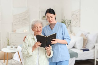 Bakıcı ve kıdemli kadın evde İncil okuyor.