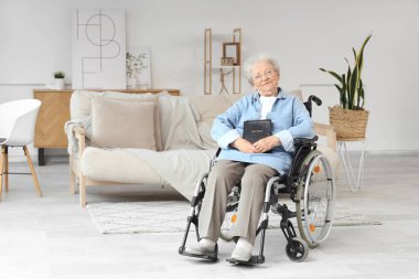 Evde İncil 'le tekerlekli sandalyede oturan yaşlı kadın.