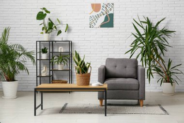 Oturma odasının iç tarafındaki beyaz tuğla duvarın yanında rahat bir koltuk, masa ve bitkiler.