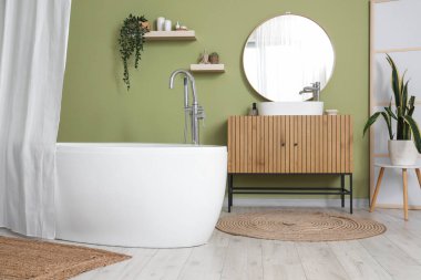 Banyonun içindeki yeşil duvarın yanındaki çekmeceleri ve perdeleri olan küvet.