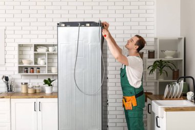 Mutfaktaki buzdolabını tamir eden mutlu erkek işçi.