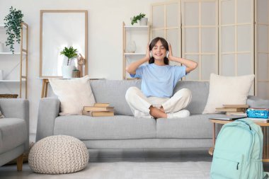 Sırt çantası ve kitaplarıyla evde oturan kulaklıklı mutlu bayan öğrenci.